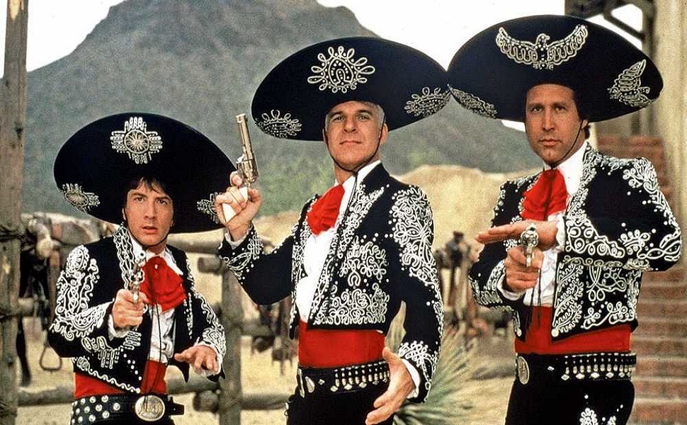 Short, Martin, and Chase are wearing elaborate mariachi-style costumes in black with white designs and matching hats. They are all holding guns.