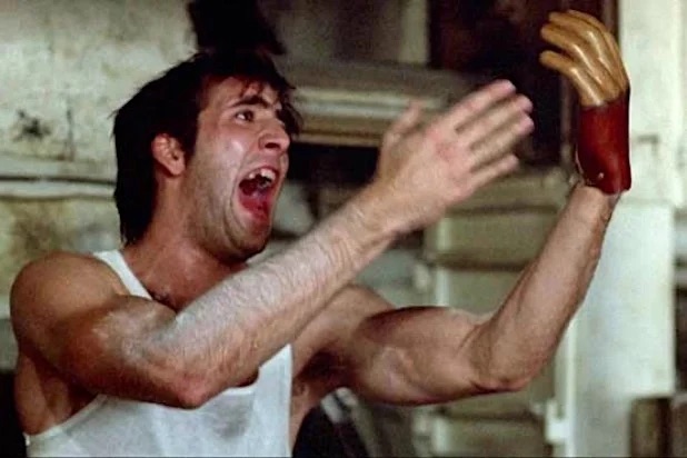 A skeevy Nicolas Cage screams at his raised wooden hand.