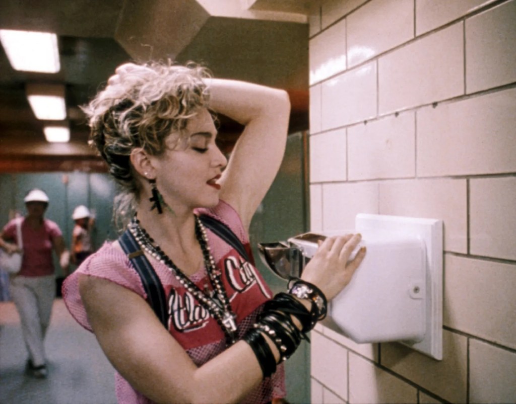Madonna dries her armpit using a bathroom hand dryer nozzle-upward.