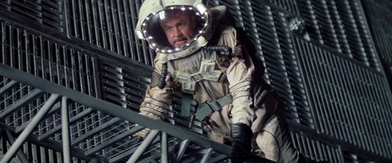 Sean Connery in a spacesuit on the outside of a ship. It looks like the face shield part of his helmet is surrounded in white LED lights.