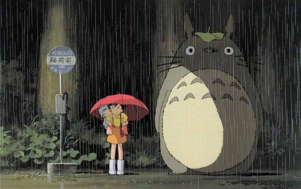 A young girl stands at a bus stop in the rain while holding an umbrella and has an even younger child on her back. She looks startled because there's a giant bunny-looking creature next to her. It's halfway between cute and honestly scary.