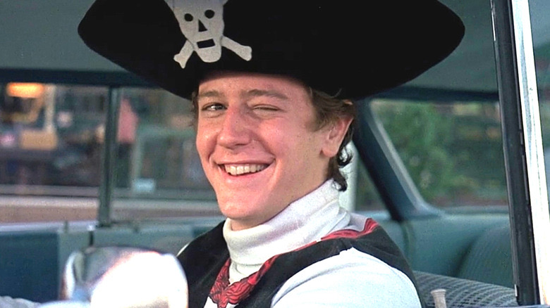 Judge Reinhold inside of a car, wearing a pirate costume and winking.