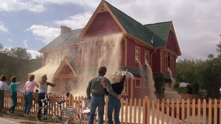 Popcorn floods out of every window of a two-story house while people look from the fence and point.