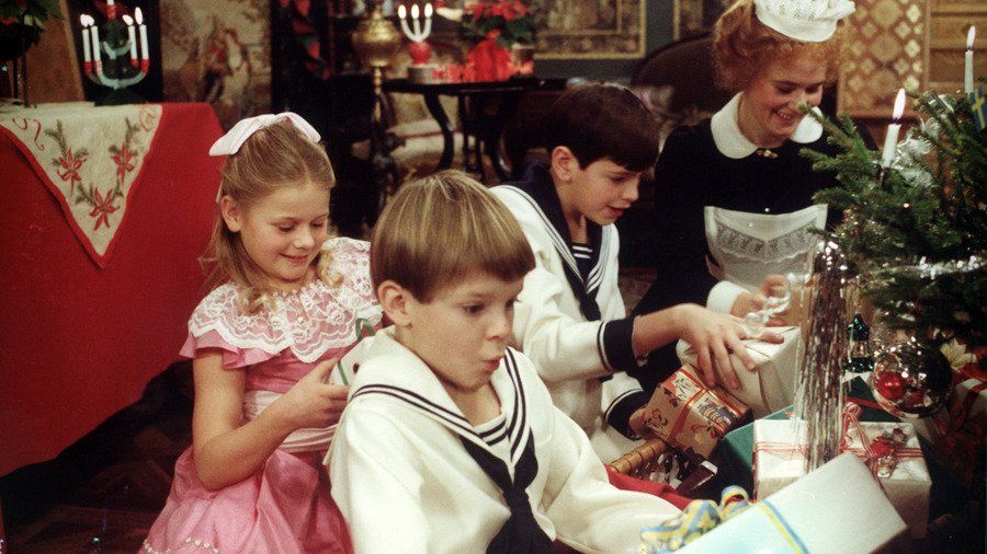 Three children–a girl in a pink dress and two boys in sailor outfits–delightedly open presents under a tree, with a maid.