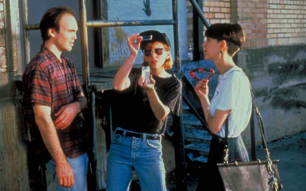 Three people stand on a street. One looks at what might be a slide? I have no idea, sorry.