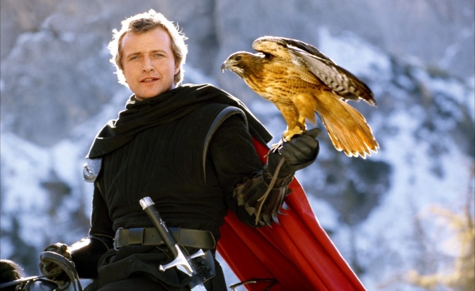 Rutger Hauer on a horse, black-clad and red-caped, holding a hawk.