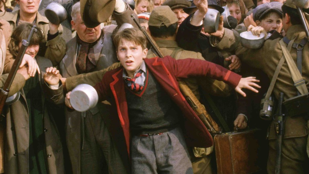 Another ragamuffin Christian Bale photo, this time holding back a crowd in a red jacket.