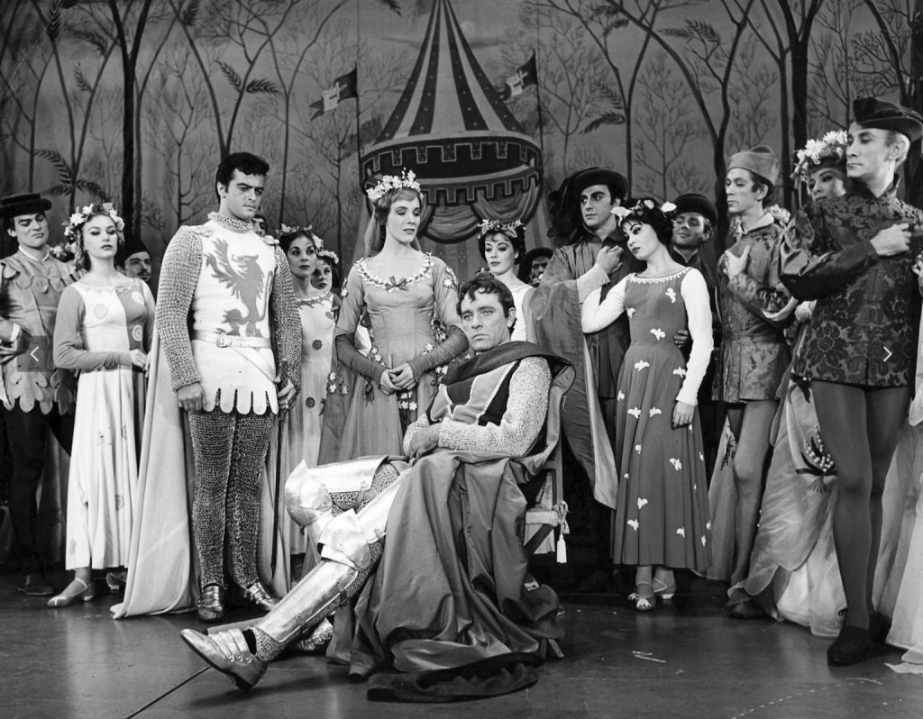 Black and white photo of the 1960 cast of Camelot. The costumes look great, Julie Andrews looks amazing, and Burton looks like he's auditioning for Hamlet, all brooding in a chair (throne?)