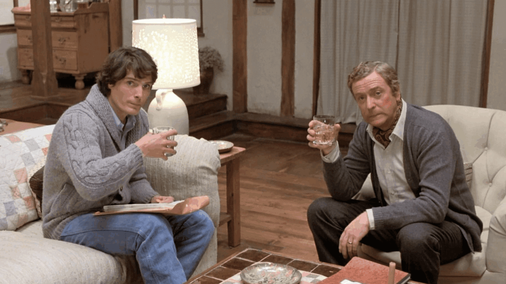 A seated Christopher Reeve and Michael Caine hold drinks and look toward the camera.