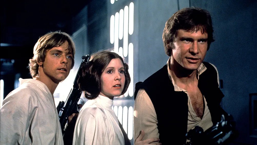 Luke, Leia (and her space buns), and Han look off-camera at something or someone. Luke and Han have guns. Excuse me, they have blasters or whatever. Han has a bit of a smile on his face but also looks suspicious at the same time. The height of Harrison Ford's acting until Shrinking, in my opinion.