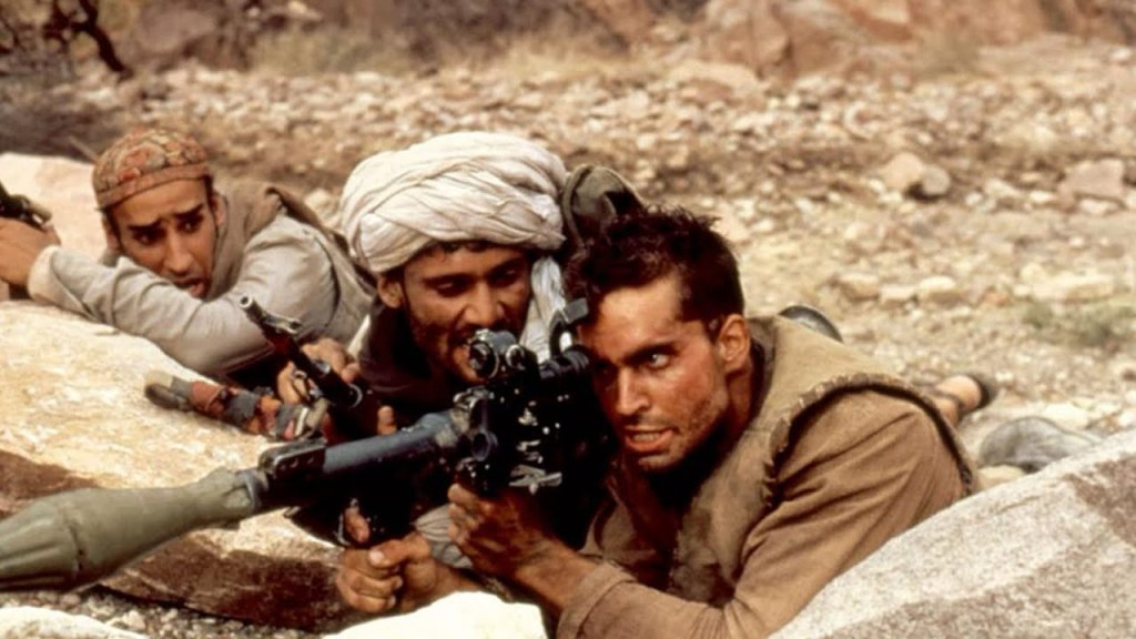 Three men lay behind light-colored rocks, as one lines up a shot on a...look, I don't know weapons. It looks like a cross between a rifle and what I think a rocket launcher is. Sorry.