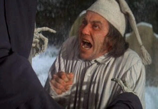 A man in a white nightgown and nightcap looks horrified as skeletal fingers reach out to him.