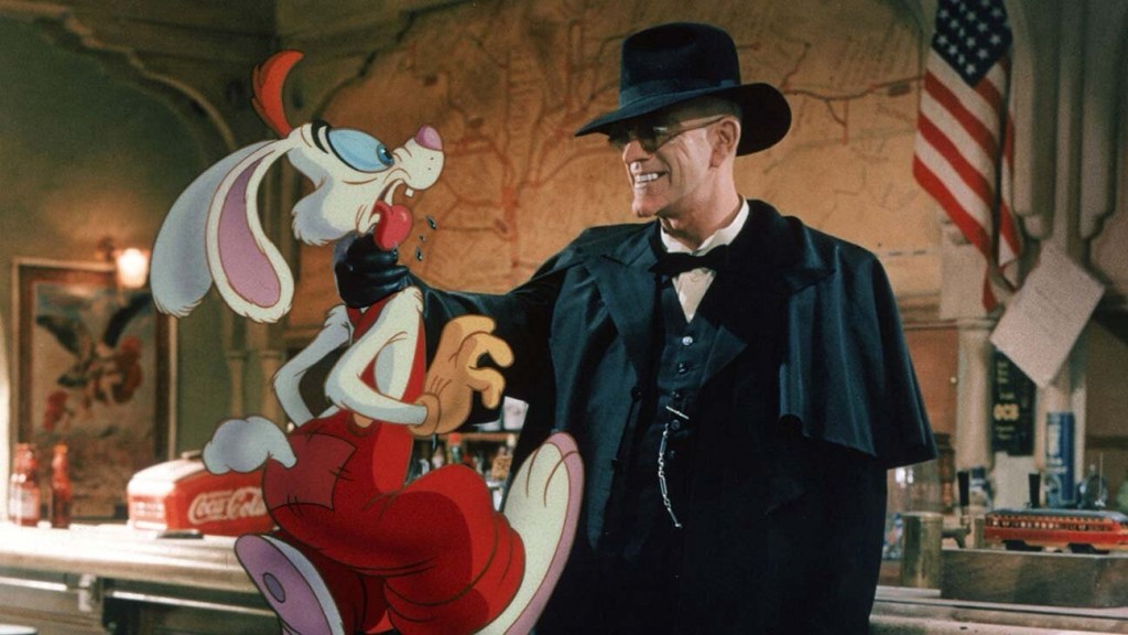 A creepy Christopher Lloyd, in all black with dark glasses, holds an animated rabbit person by the throat.