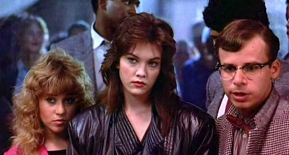 A woman with feathery dark hair and a leather jacket has a blonde woman and Rick Moranis on each side of her.