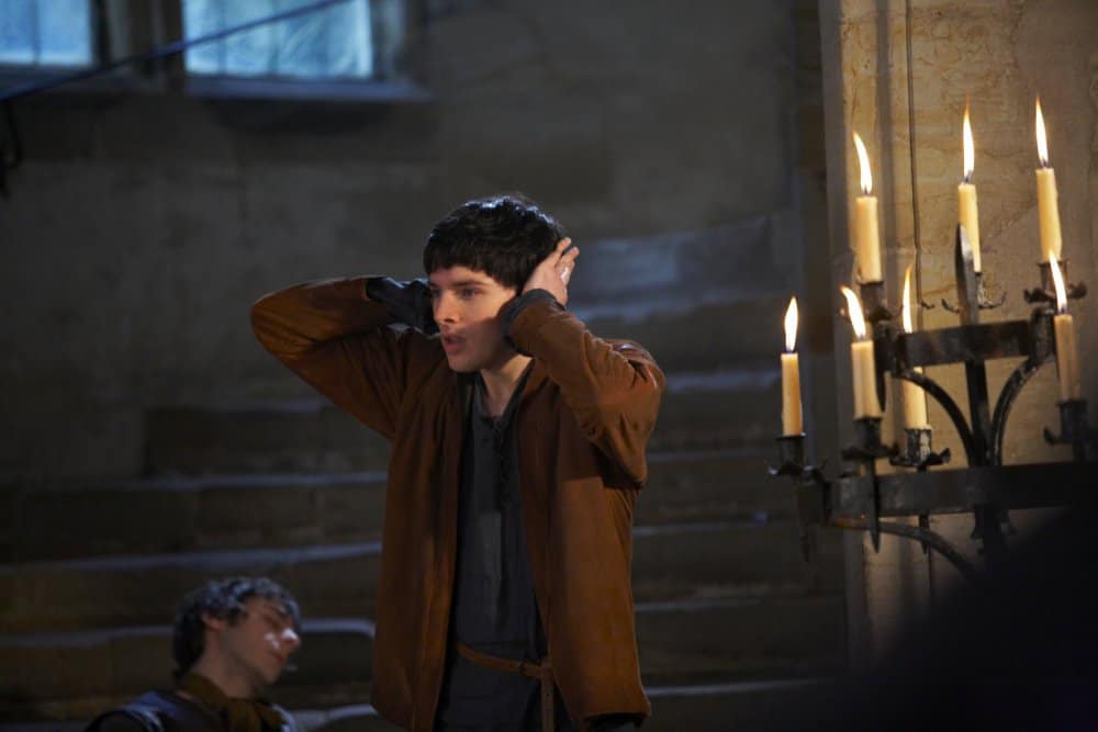 A young man with a terrible bowl haircut covers his ears inside a castle.