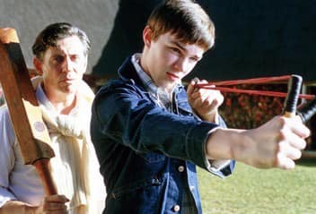 A young Nicholas Hoult aims a slingshot while Gabriel Byrne stands behind him, holding a cricket bat. Probably not as ominous as I make it sound.