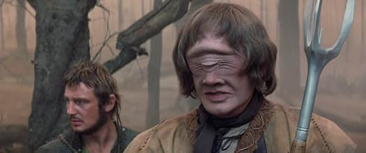 A young Liam Neesom with a sort of ecopunk version of his Star Wars hair and a Cyclops holding a cross between a pitchfork and one of those pickle forks. They're in a swamp, maybe. The background is very tan.