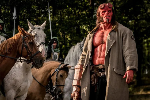 Hellboy, a red demon guy with very abs, is around some horses. Sorry, he's not as hot as Ron Perlman.
