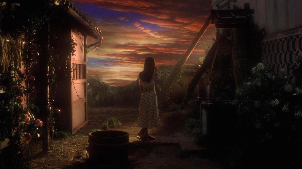 A young woman in a dress faces away from the camera, towards a stunning sky. She stands between two buildings, and there's something very Wizard of Oz going on here. I dunno, I haven't seen the movie.
