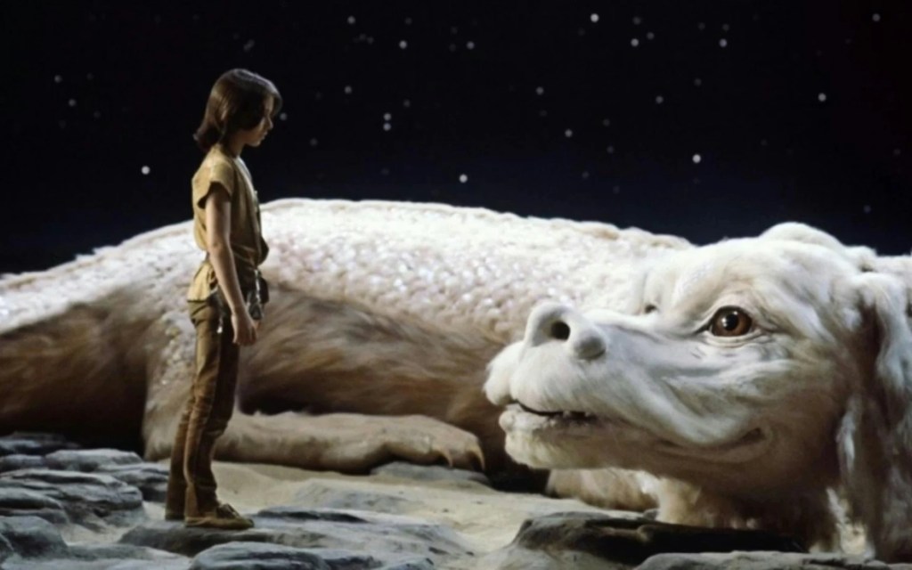 A boy with longish brown hair stands before a giant, off-white dog-looking creature. Behind them is the night sky. Beneath them is rocks and sand.