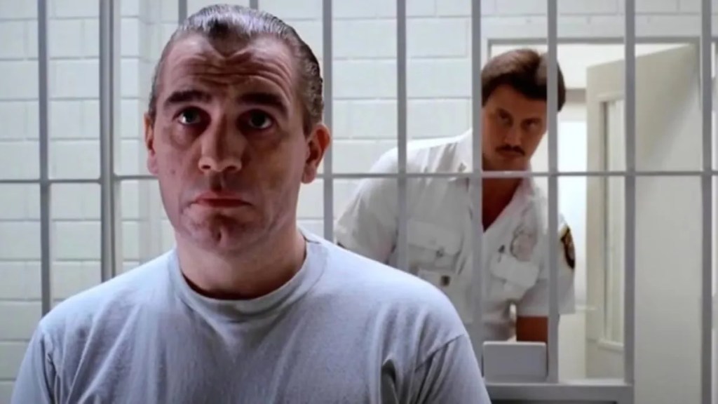 Two white men, one behind bars (on the side closest to the camera), one in uniform on the other side, everything is white