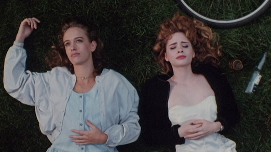 Two young white women lay in the grass on their backs, their hair spread around them. Part of a bicycle tire is in the top corner.