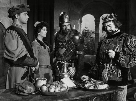 Black and white still of medieval or whenever people around a table. One man has a crown on his head, one is very much a knight.