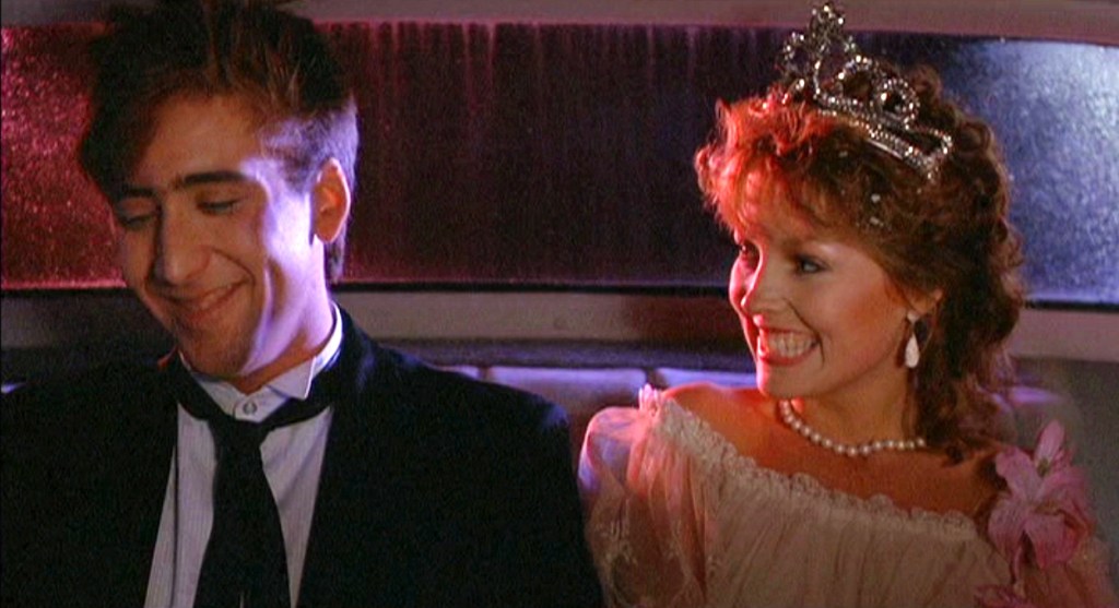 Nicolas Cage, smiling, dimpled, and looking down, the best I've ever seen him look, next to a beautiful Deborah Foreman in a tiara with the biggest smile