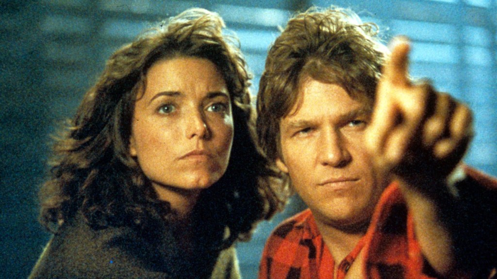 A white man in a red flannel shirt points into the distance while a white woman looks where he's pointing