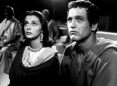 A man and woman in black and white look off camera at the same thing. He is dressed plainly. She is wearing some very pretty jewelry.