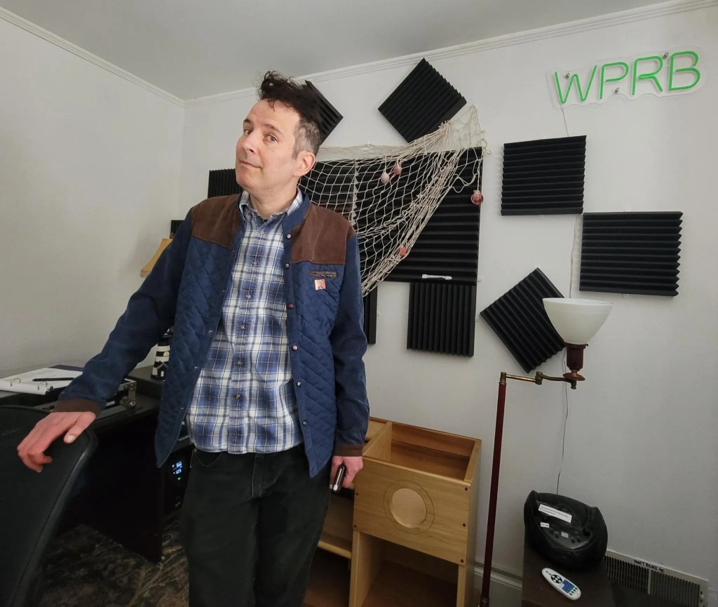 A middle-aged white man with soundprooding behind him and the letters on the wall read WPRB