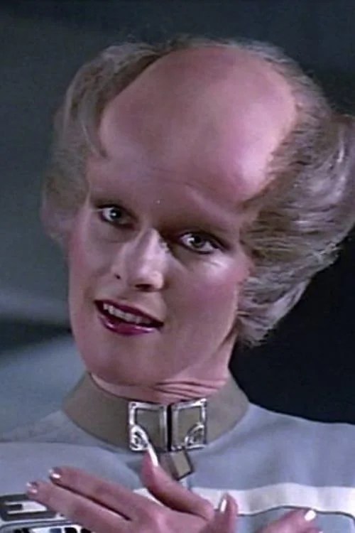This person must be an alien, because it was the 80s and there seems to maybe be some gender fuckery afoot. For example, this person has lipstick and eyeliner but the most dad growing out his hair a little because the top is all gone haircut. Big brained, I suppose, because there's a bit of a noticeable ridge around the bald spot. Also they are wearing a lock around their neck, so a kinky alien?