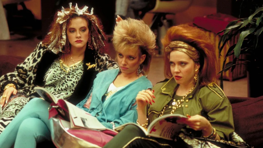 Three young women in a hair salon. One, Joan Cusack, has foils in her hair and wears what might be a white leopard-print jumpsuit, with what looks like a knit leopard-print cardigan, with what might be a leopard pin. Another has short blonde hair except her hair is so tall I don't know if I can rightfully call it short. Another is wearing what I want to call military athlesiure and her high, unnaturally red hair is held back with a thick gold wrap-headband. Her roots are rounded above the headband. It could not be more 80s or more tacky.