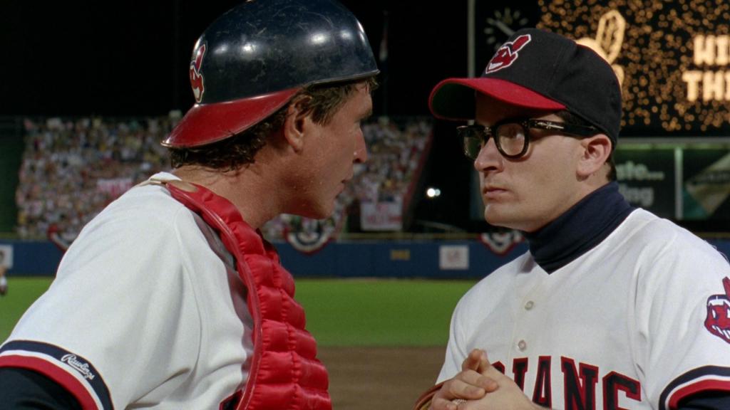 Two baseball players look at each other intently. One wear extra padding and one has thickly-framed black glasses.
