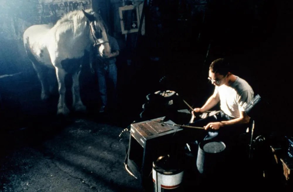A person plays makeshift drums next to a white horse