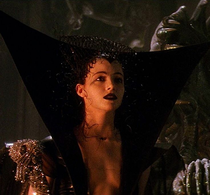 Mia Sara wearing a black dress cut so wide and deep that Star Sapphire is jealous. She has on dark lipstick and a strange black headdress...thing...and it's all very otherworldly and kinda evil.